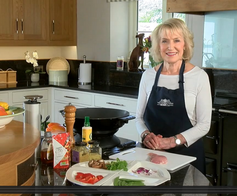Rosemary Conley standing behind a kitchen worktop holding the ingredients of a chicken stir-fry