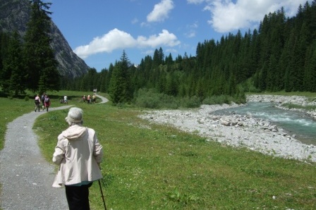 View of walkers spread out along a scenic path beside a river next to a mountain