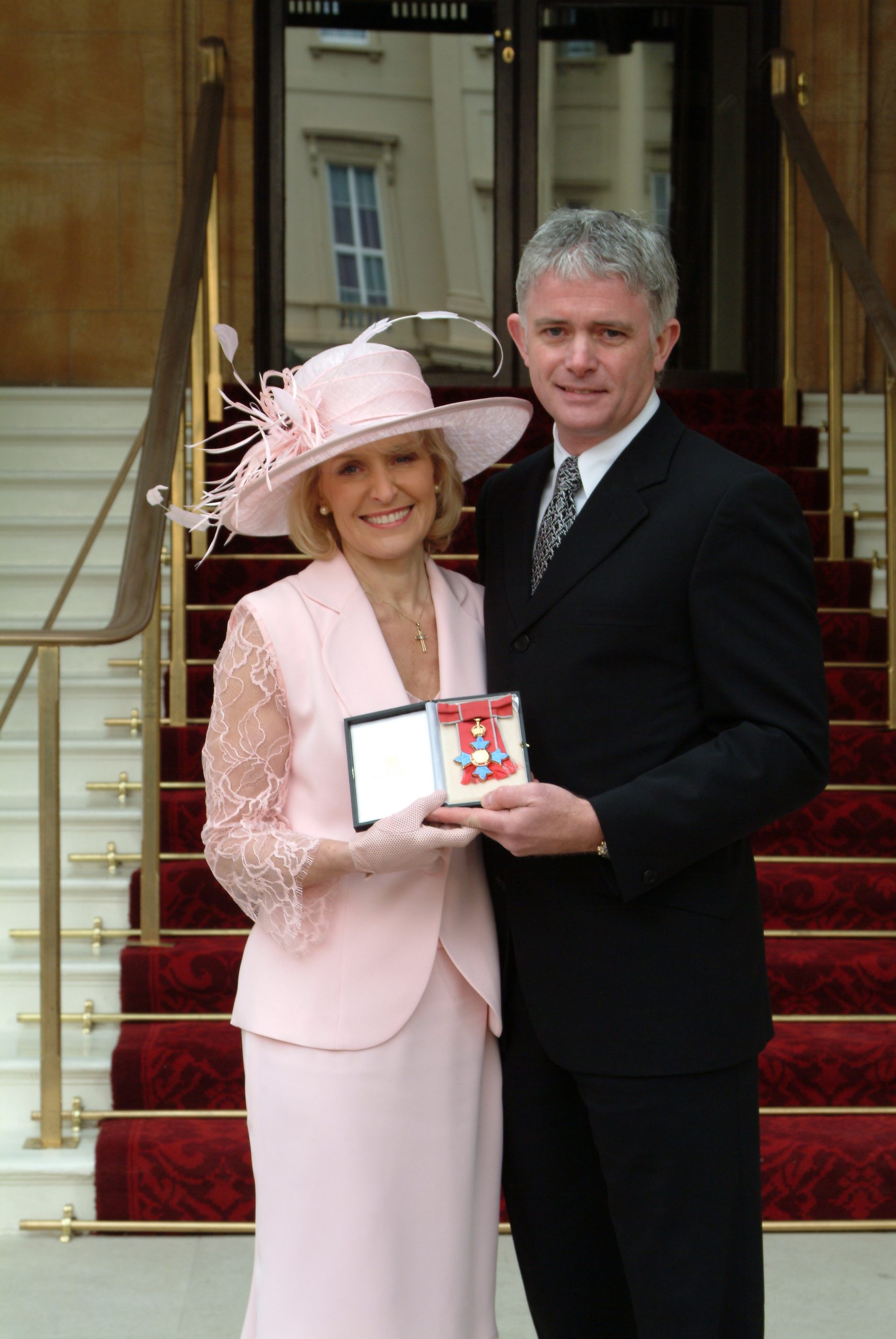 Rosemary Conley and husband Mike Rimmington on the steps of Buckingham Palace holding her CBE