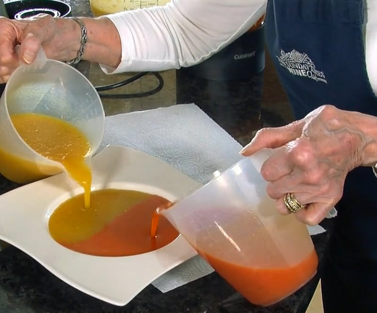 Two jugs of different coloured soups being poured simultaneously into either side of a bowl