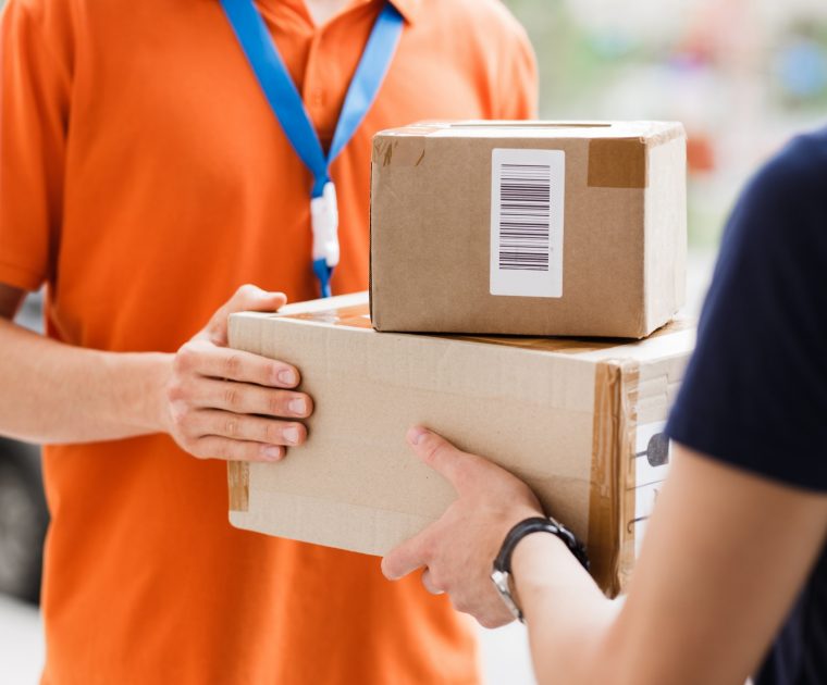A person wearing an orange T-shirt and a name tag is delivering parcels to a client. Great parcel deliveries start with learning the names of your regular delivery drivers.