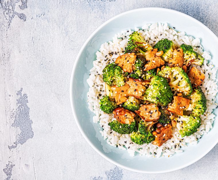 A round dish of fried tempeh and broccoli on a bed of white rice