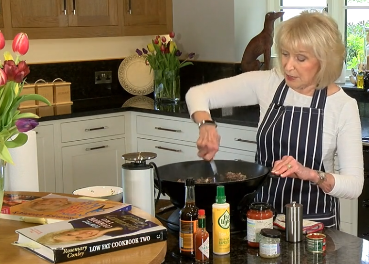Rosemary Conley stiring a spaghetti bolognese cooking in an electric wok on the kitchen worktop