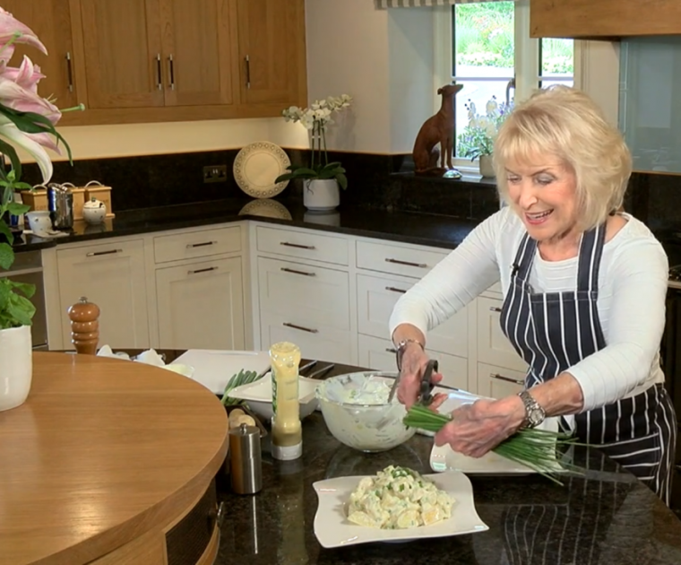 Rosemary Conley snipping some spring onions onto a dish of Potato Salad in her kitchen
