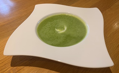 Roasted garlic and green pea soup in a white bowl with a swirl of yoghurt