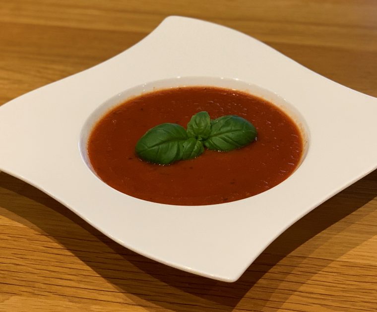 Easy Tomato and Roasted Garlic Soup in a white bowl topped with a sprig of basil