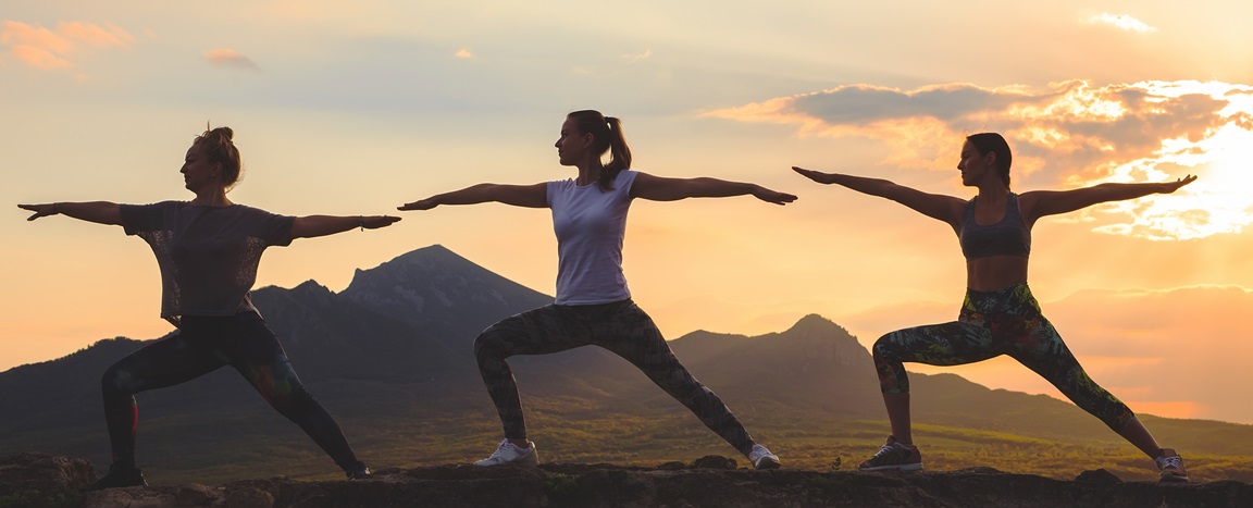 Silhouette of young womans practicing pilates at sunset or sunrise in beautiful mountain location.