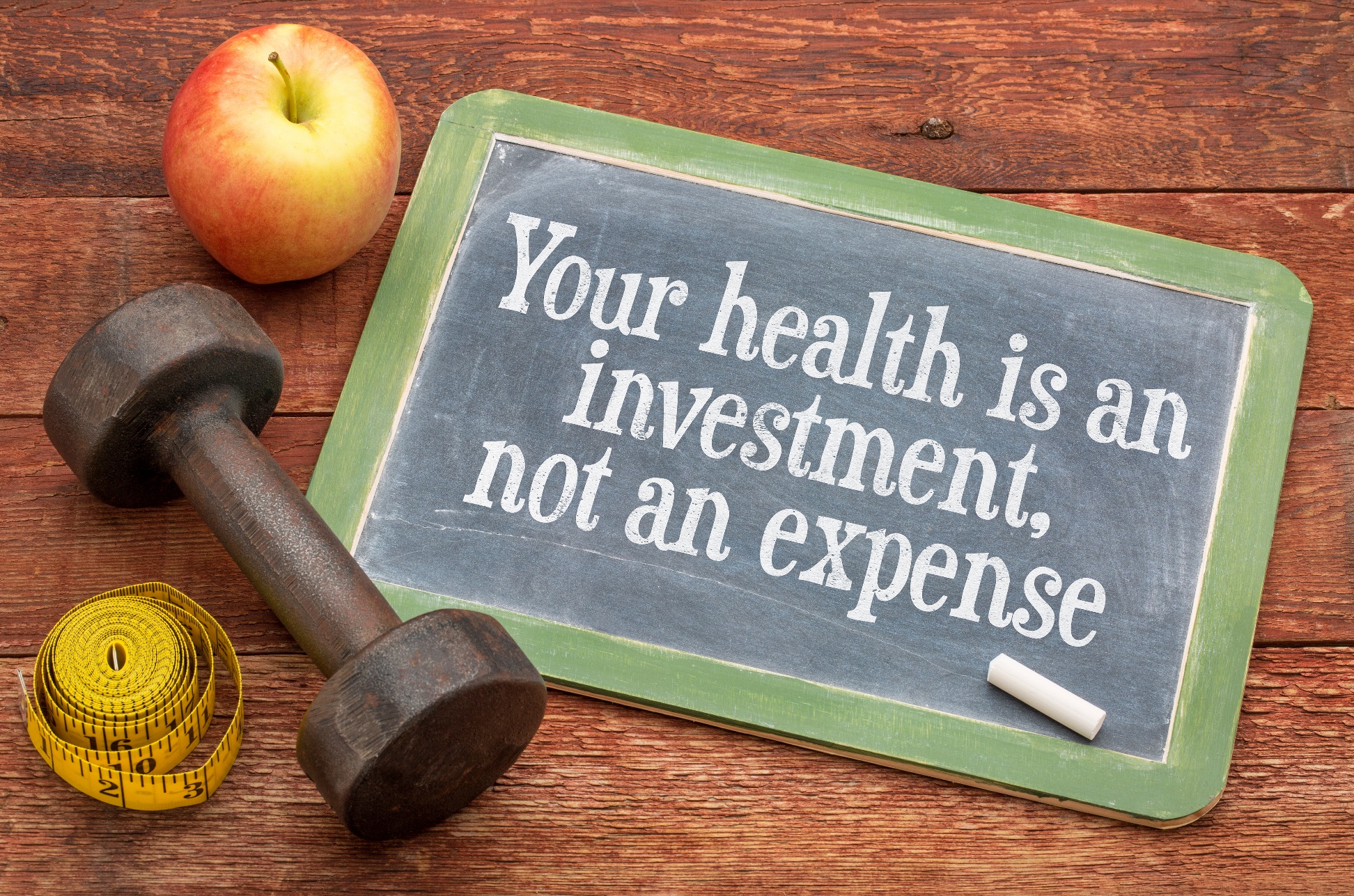 Health is an investment not an expense written on a blackboard on a wooden table with an apple, a tape measure and a small exercise hand-weight