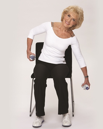 Rosemary Conley sat on a chair exercising with a waterbottle as a weight in each hand.