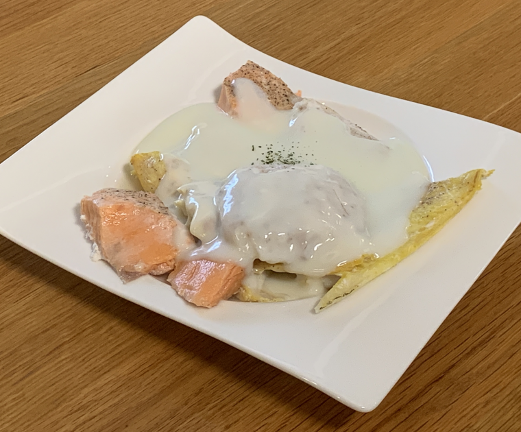 A medley of fresh cod, smoked haddock and salmon arranged on a white plate smothered in a white sauce.