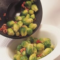Tender green Brussells Sprouts mixed with crispy pancetta being poured out of a pan into a serving dish