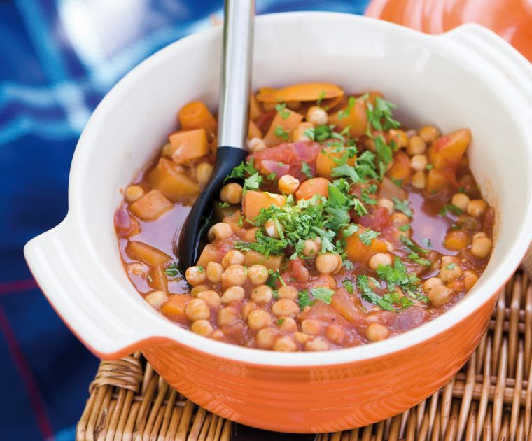 Chickpea and Root Vegetable Stew in an orange casserole dish. The chickpeas and chunks of swede and carrot are topped with chopped parsley