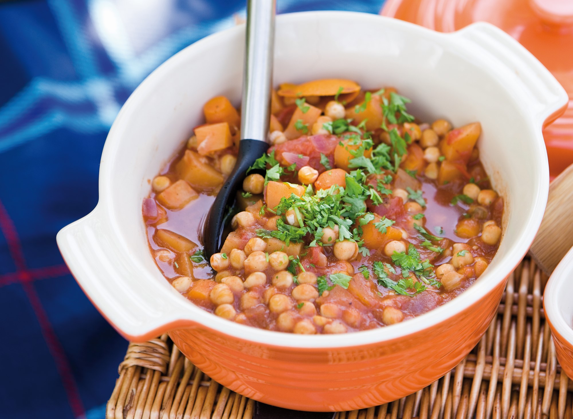 Chickpea and Root Vegetable Stew in an orange casserole dish. The chickpeas and chunks of swede and carrot are topped with chopped parsley