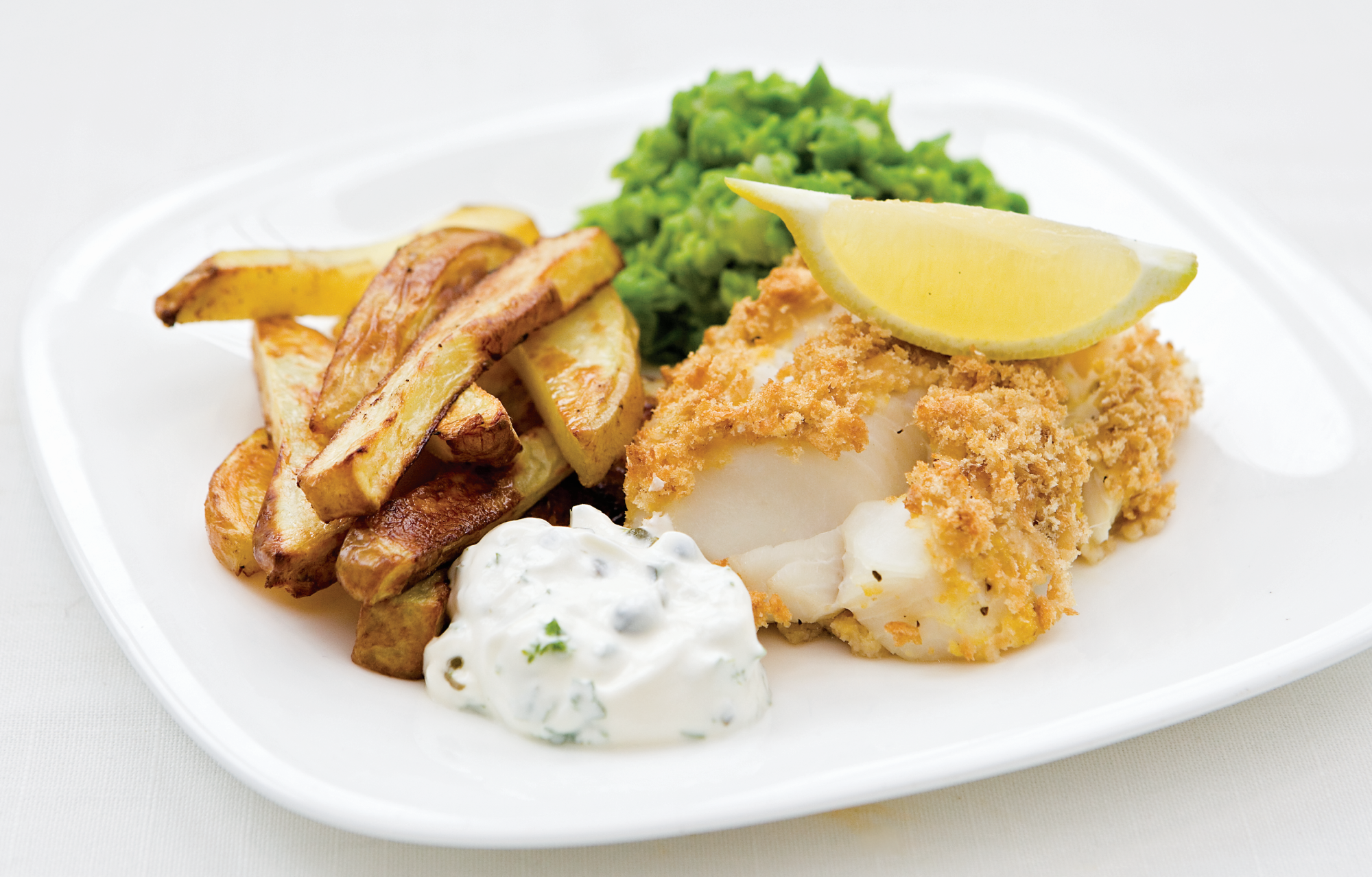 A fillet of cod in homemade breadcrumbs with a lemon wedge on top, served with home-made chips, lightly mushed garden peas and a blob of home-made tartare sauce.