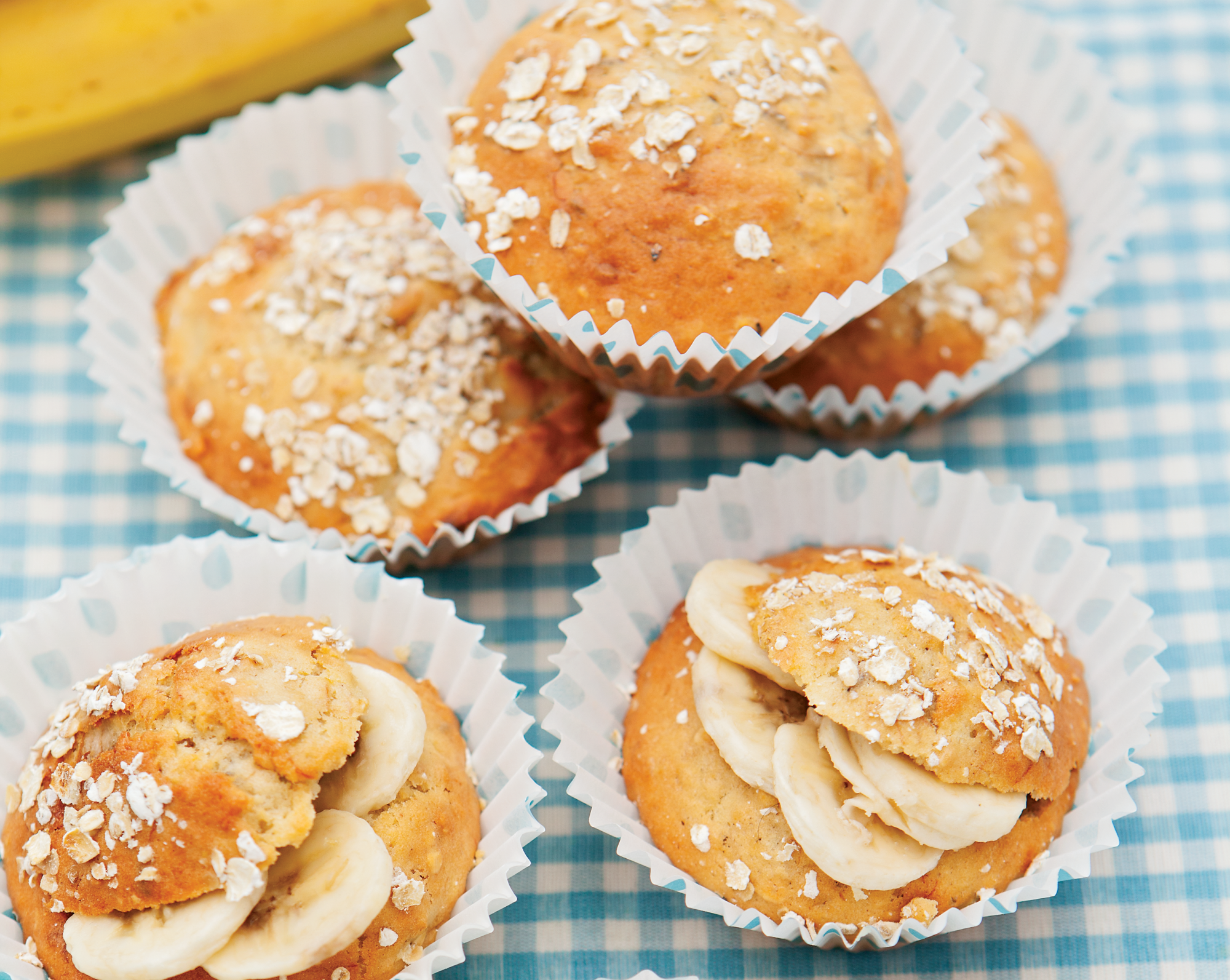 Banana Muffins in paper cases. Some are decorated by being sprinkled with oats, others have a slit containing slices of banana in the top.