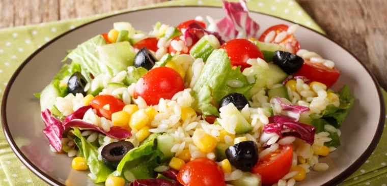 A colourful plate of Rice Salad made with white rice, chopped cherry tomatoes, sweetcord, chopped olives and chopped salad leaves.