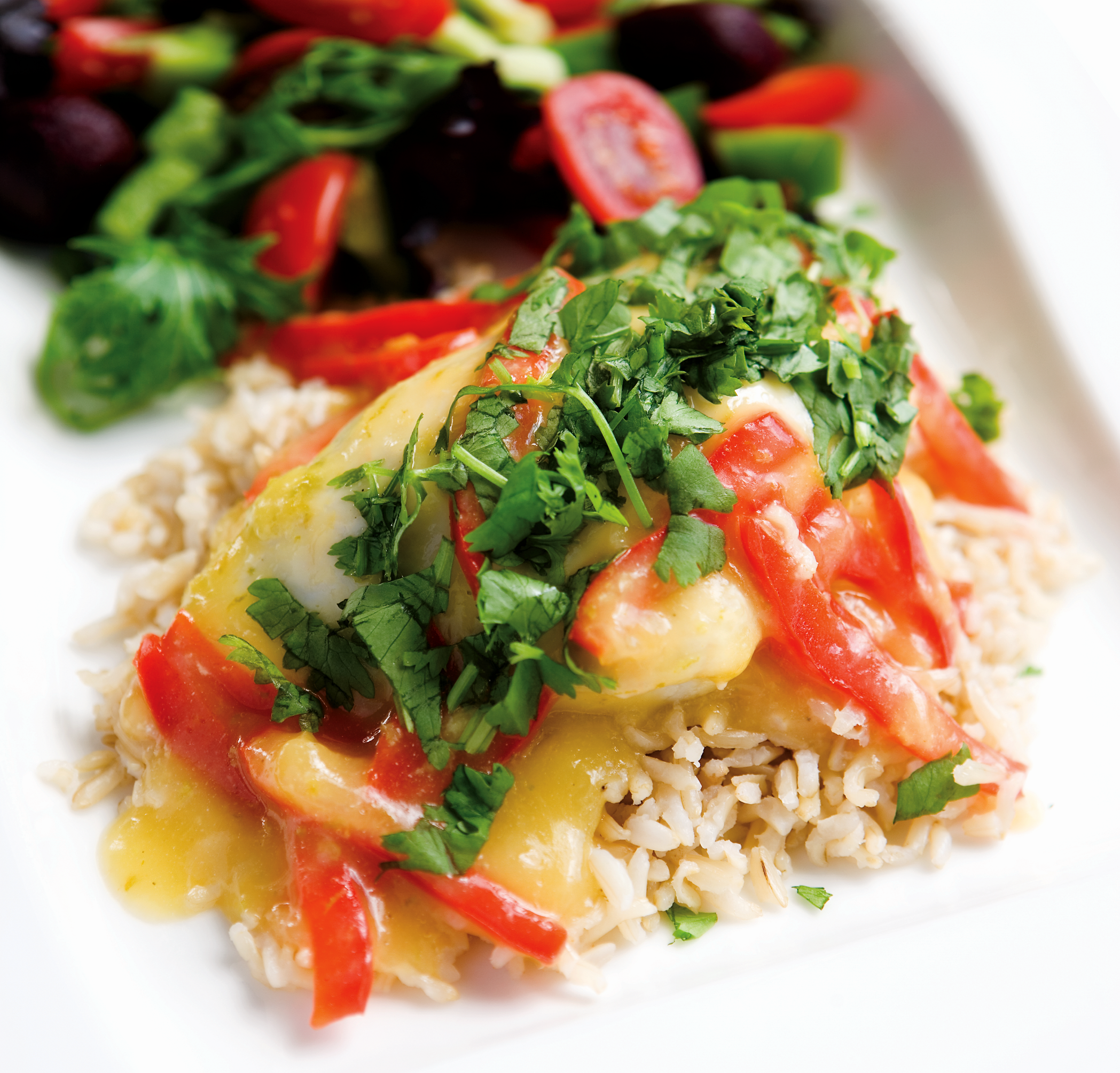 A plate of sweet chilli chicken on a bed of white rice with a mixed salad