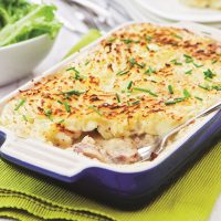 Sausage and Mushroom Pie in a blue oven-proof casserole dish showing the creamy saudage and mushroom filling topped with a golden baked mash topping sprinkled with chives.