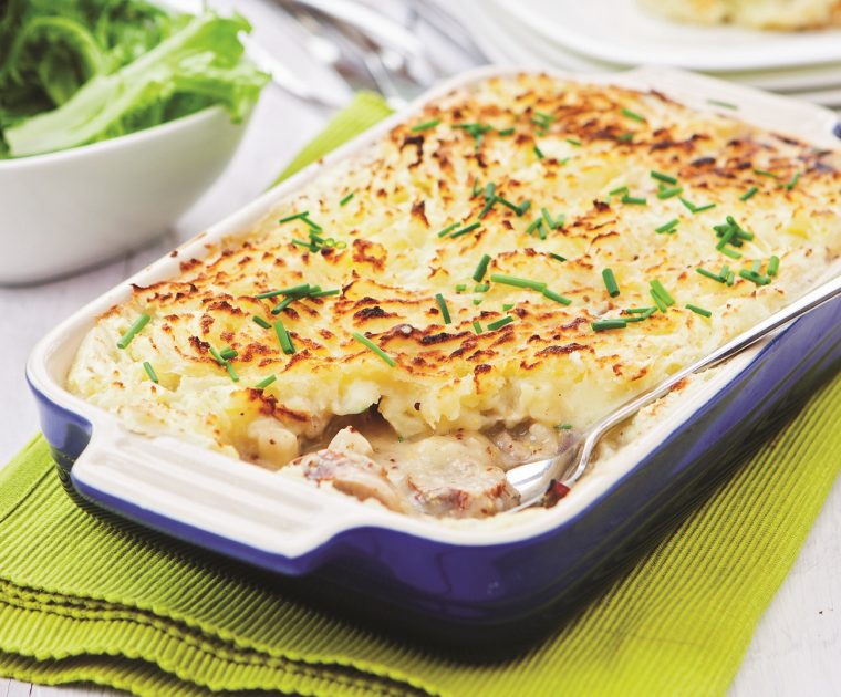 Sausage and Mushroom Pie in a blue oven-proof casserole dish showing the creamy saudage and mushroom filling topped with a golden baked mash topping sprinkled with chives.