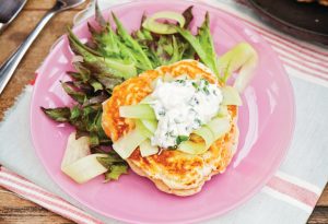Smoked Salmon drop scones on a pink plate topped with a creamy suace and served with a side salad of green leaves as a light lunch