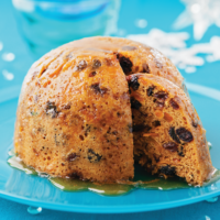 Black Cherry and Mango Christmas Pudding is an alternative to a traditional dark Christmas pudding with a lighter coloured sponge and a different flavoured fruit filling. It's shown here drizzled in manouka honey and sat on a blue glass plate.