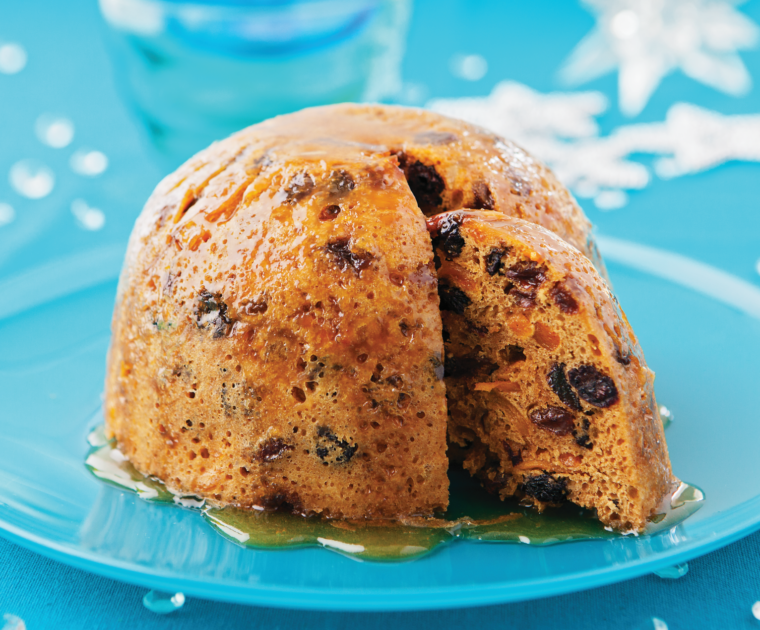 Black Cherry and Mango Christmas Pudding is an alternative to a traditional dark Christmas pudding with a lighter coloured sponge and a different flavoured fruit filling. It's shown here drizzled in manouka honey and sat on a blue glass plate.