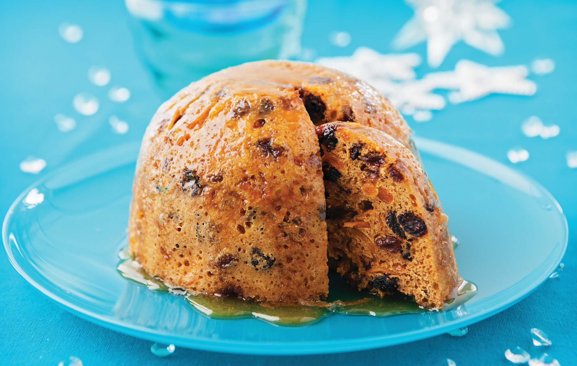 Black Cherry and Mango Christmas Pudding is an alternative to a traditional dark Christmas pudding with a lighter coloured sponge and a different flavoured fruit filling. It's shown here drizzled in manouka honey and sat on a blue glass plate.