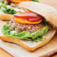 A duck and pork burger served in a bun with lettuce, a slice of orange and quince.