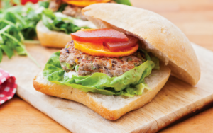A duck and pork burger served in a bun with lettuce, a slice of orange and quince.