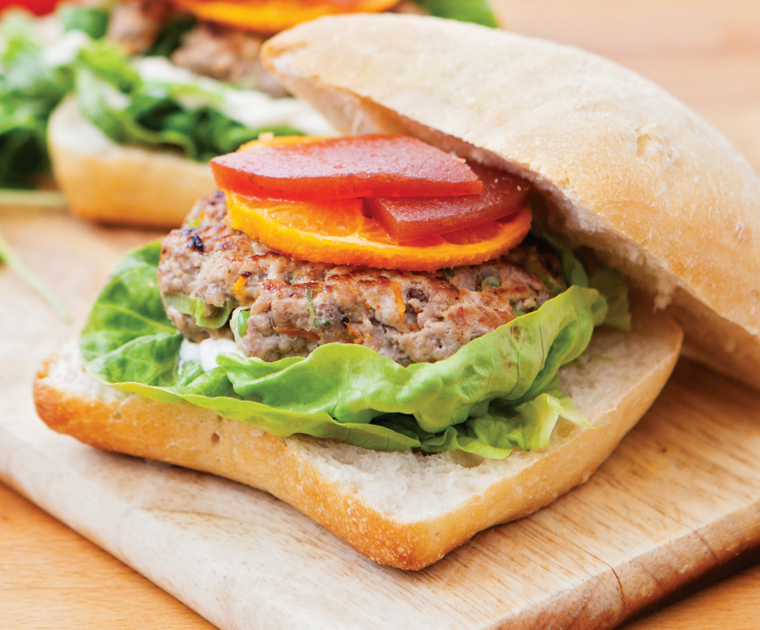 A duck and pork burger served in a bun with lettuce, a slice of orange and quince.