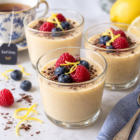 A small glass of Earl Grey and Lemon Tea custard dessert topped with a couple of blueberries and raspberries and some gratings of lemon zest and dark chocolate
