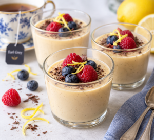 A small glass of Earl Grey and Lemon Tea custard dessert topped with a couple of blueberries and raspberries and some gratings of lemon zest and dark chocolate
