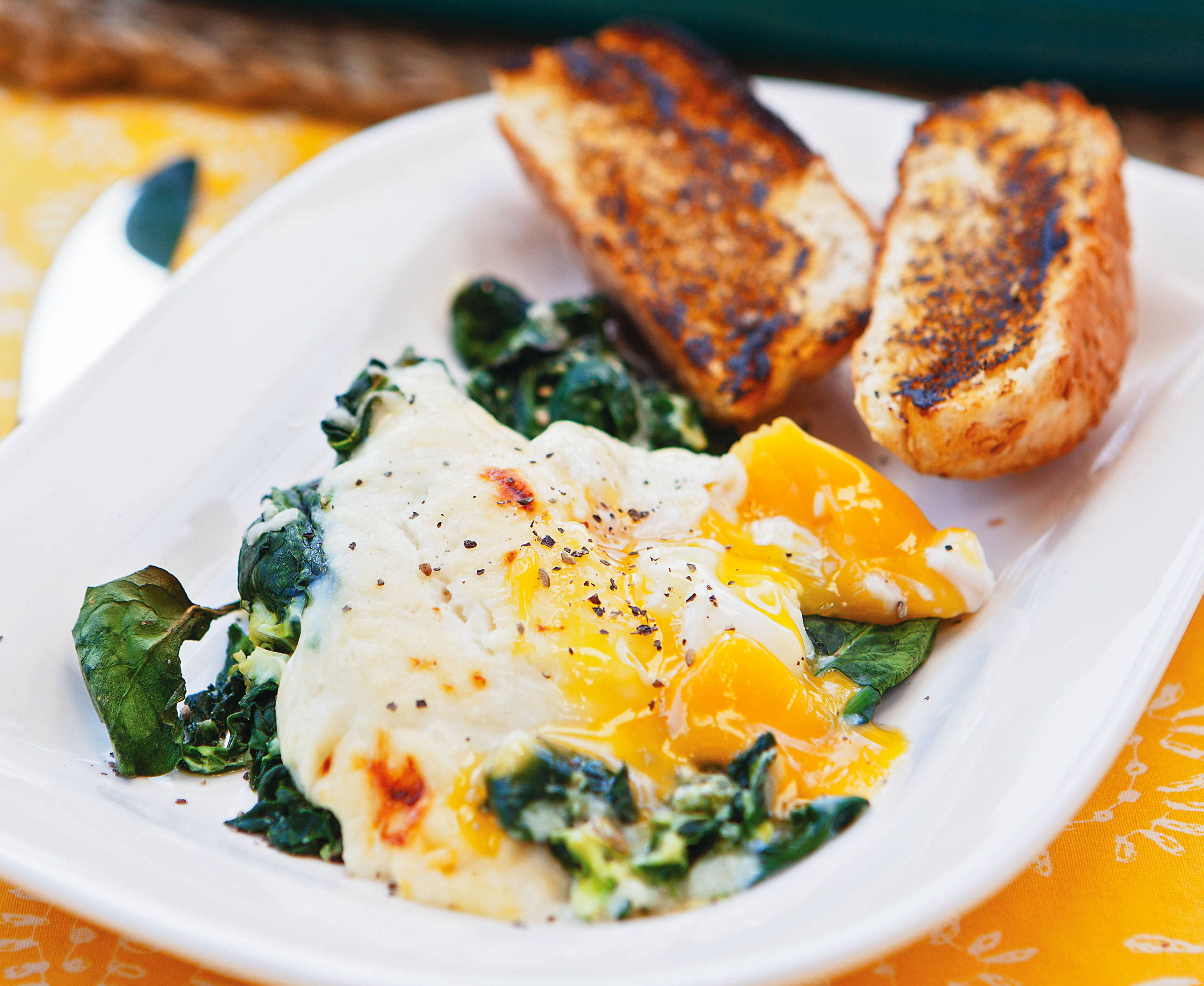 Eggs Florentine is a golden yolked egg sitting on a bed of wilted spinach smothered in a mustard and cheese sauce. It is served with a toasted bread bun.