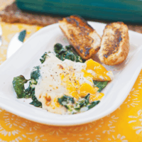Eggs Florentine is a golden yolked egg sitting on a bed of wilted spinach smothered in a mustard and cheese sauce. It is served with a toasted bread bun.
