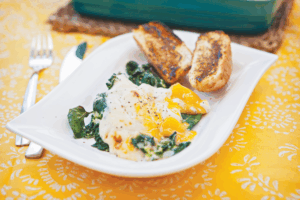 Eggs Florentine is a golden yolked egg sitting on a bed of wilted spinach smothered in a mustard and cheese sauce. It is served with a toasted bread bun.