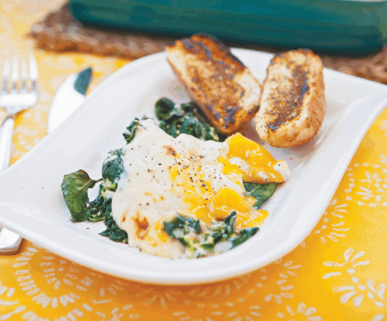 Eggs Florentine is a golden yolked egg sitting on a bed of wilted spinach smothered in a mustard and cheese sauce. It is served with a toasted bread bun.