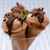 Low-fat home-made chocolate mint ice cream, made from greek yogurt, custard and cocoa powder, in a wafer cone topped with melted chocolate and decorated with a mint leaf.