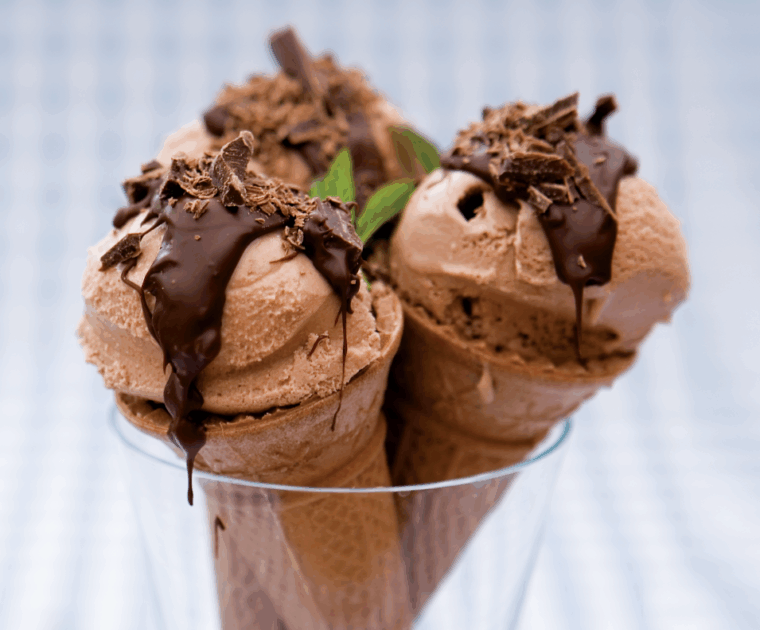 Low-fat home-made chocolate mint ice cream, made from greek yogurt, custard and cocoa powder, in a wafer cone topped with melted chocolate and decorated with a mint leaf.