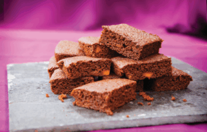 Pumpkin Parkin, a ginger-bread style tray-bake, cut into squares and stacked ona grey slate chopping board