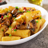 A bowl of Rigatoni Pasta Miso and Chilli Mushrooms. Rigatoni pasta tubes in a glistening sauce made from miso paste, white wine and sesame oil with chestnut mushrooms sprinkled with chilli and fennel seeds.