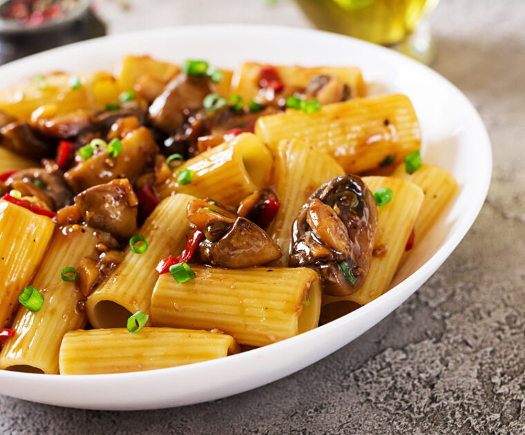 A bowl of Rigatoni Pasta Miso and Chilli Mushrooms. Rigatoni pasta tubes in a glistening sauce made from miso paste, white wine and sesame oil with chestnut mushrooms sprinkled with chilli and fennel seeds.
