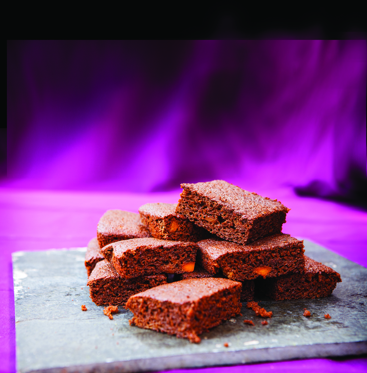 Pumpkin Parkin, a ginger-bread style tray-bake, cut into squares and stacked ona grey slate chopping board